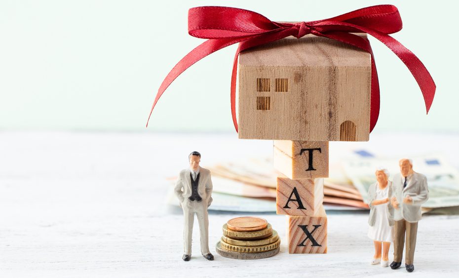 maison jouet en bois sur les lettres TAX représentant l'héritage immobilier